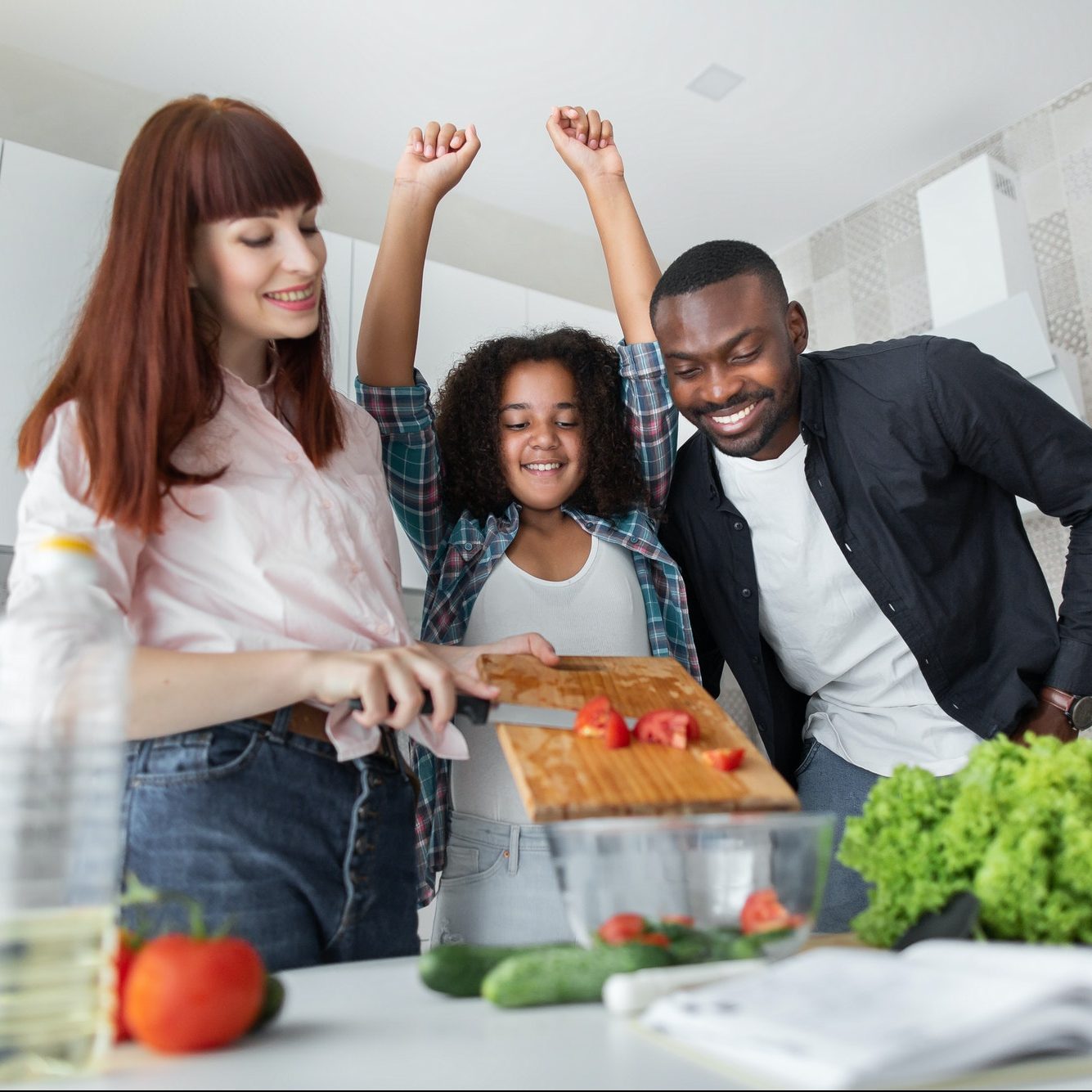 Multiethnic joyful family with mixed race daughter preparing vegetable salad at kitchen at home